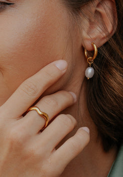 Close-up of a person wearing gold hoop earrings with a pearl accent and matching ring.