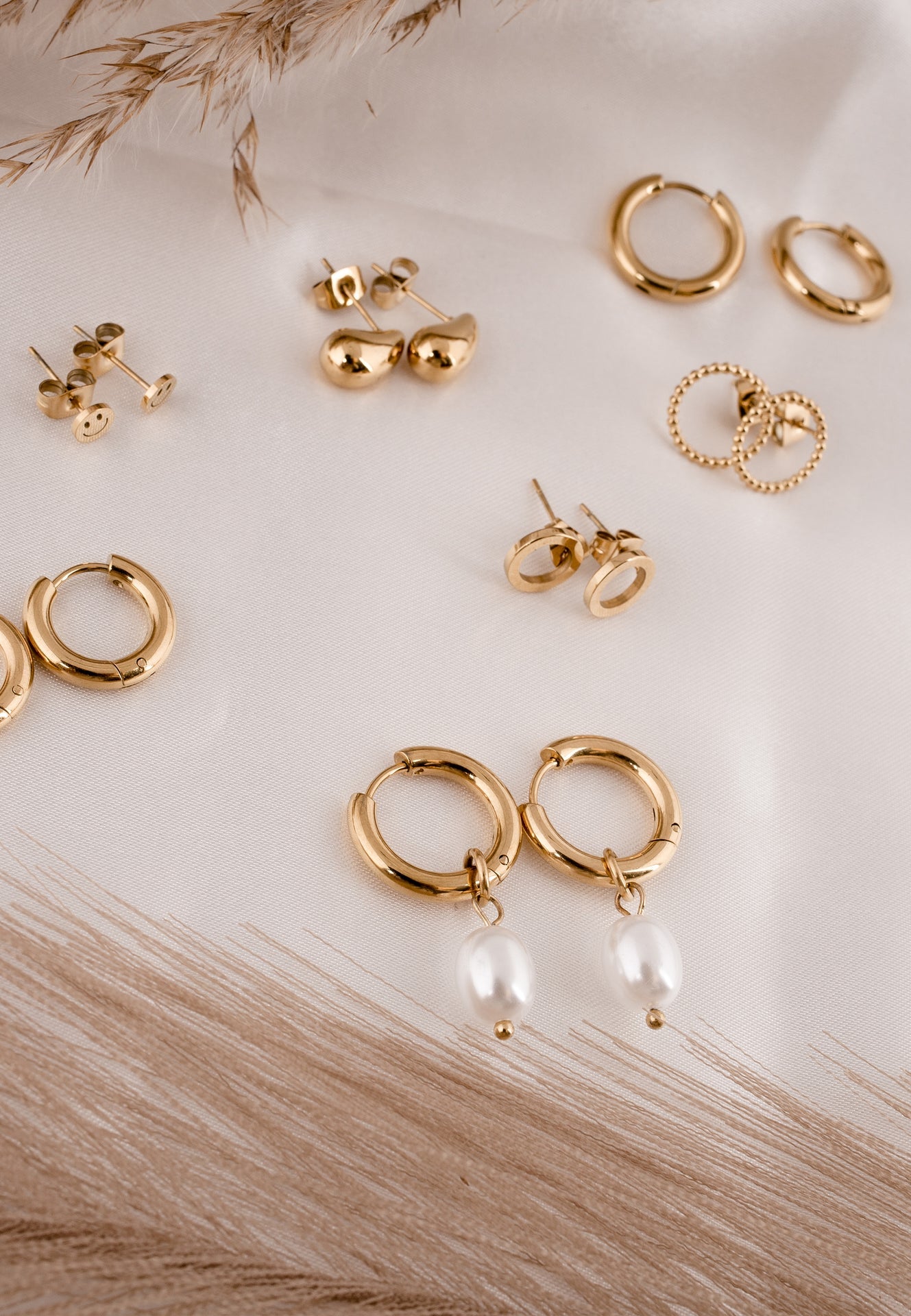Collection of gold earrings on a light wooden surface with dried grasses.