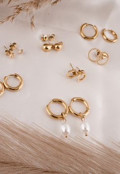 Collection of gold earrings on a light wooden surface with dried grasses.