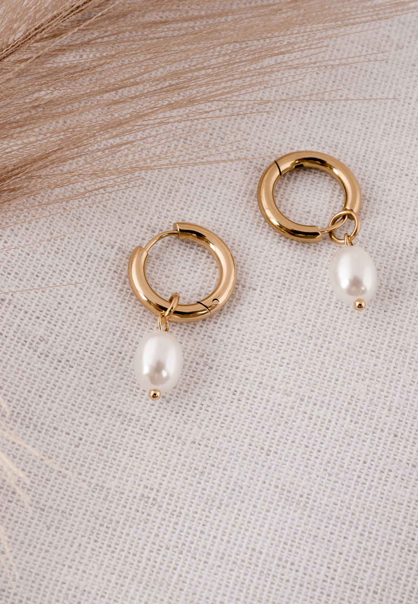 Gold hoop earrings with pearl drops on a textured fabric background