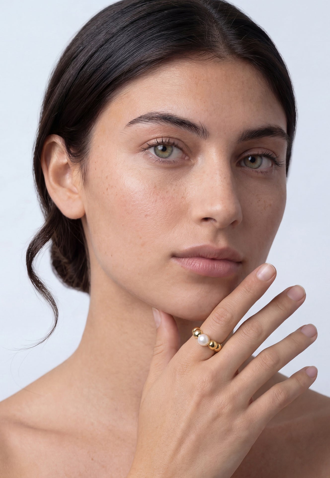Woman wearing a gold ring with a pearl on a plain background
