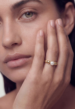 Close-up of a woman's face with a pearl ring on her finger
