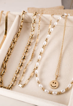 Gold necklaces with pearls and a smiley face charm on a beige surface
