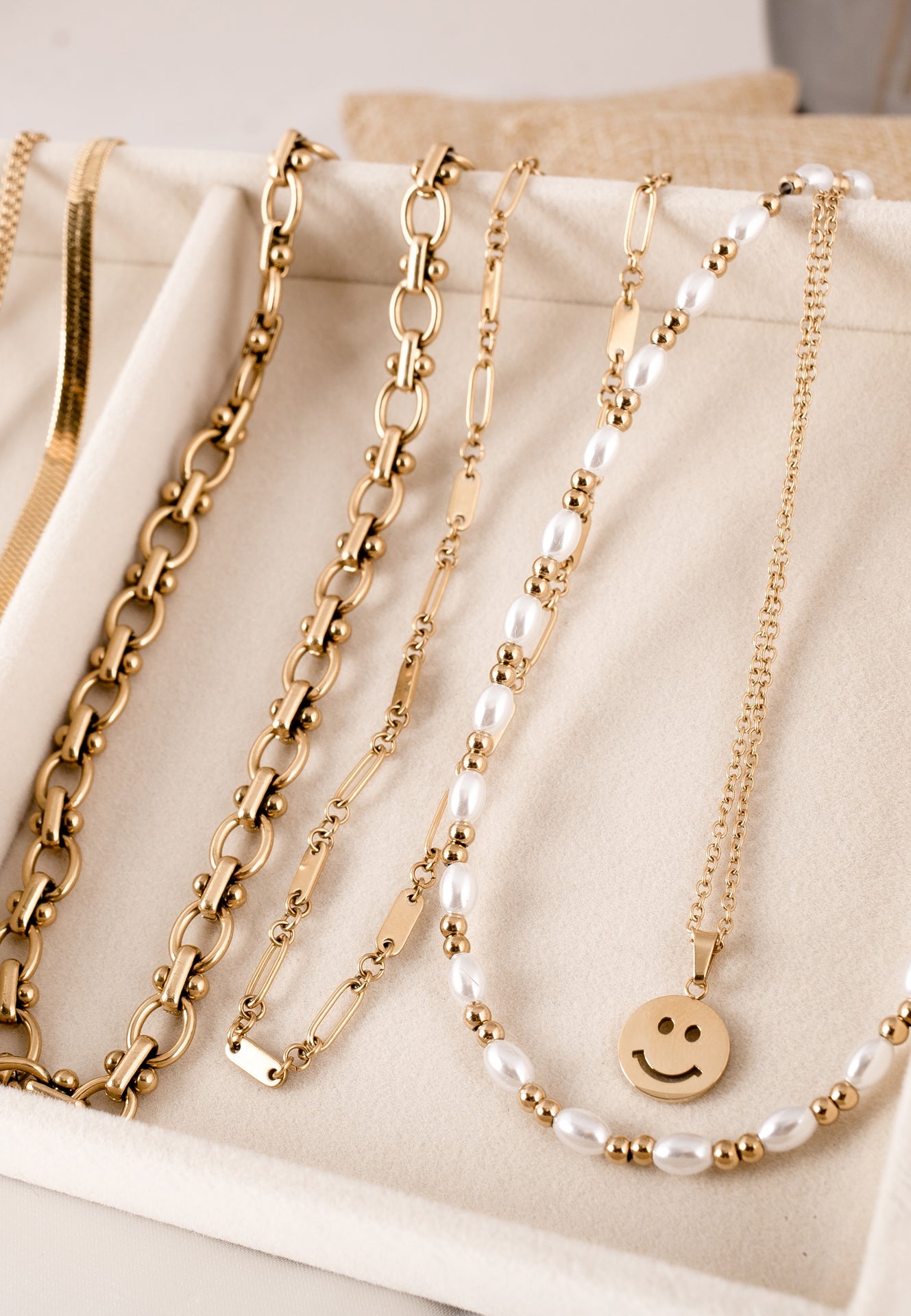 Gold necklaces with pearls and a smiley face charm on a beige surface