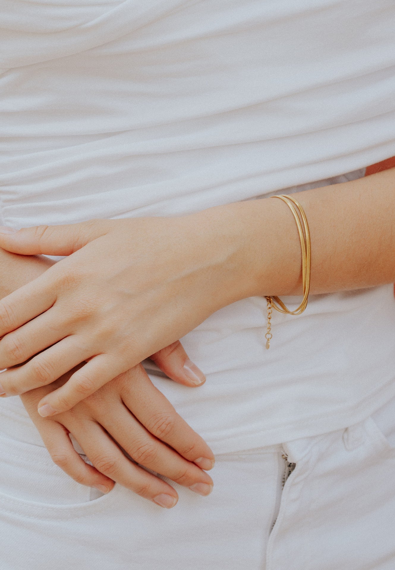Close-up of a hand wearing gold bracelets on a light background