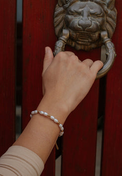 Hand with a pearl bracelet reaching for a lion head doorknocker on a red door.
