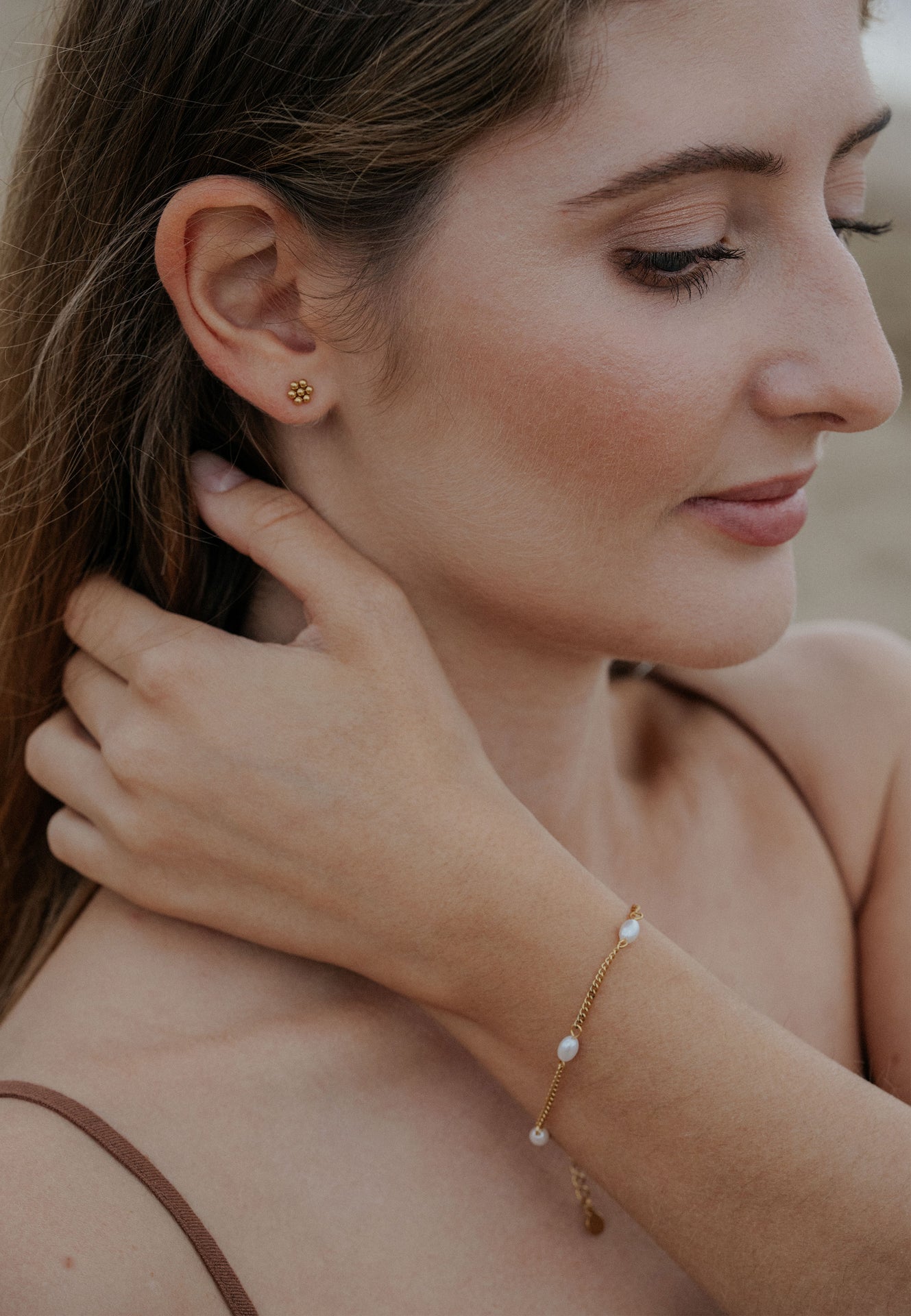 Woman wearing gold earrings and bracelet, close-up of face and hand