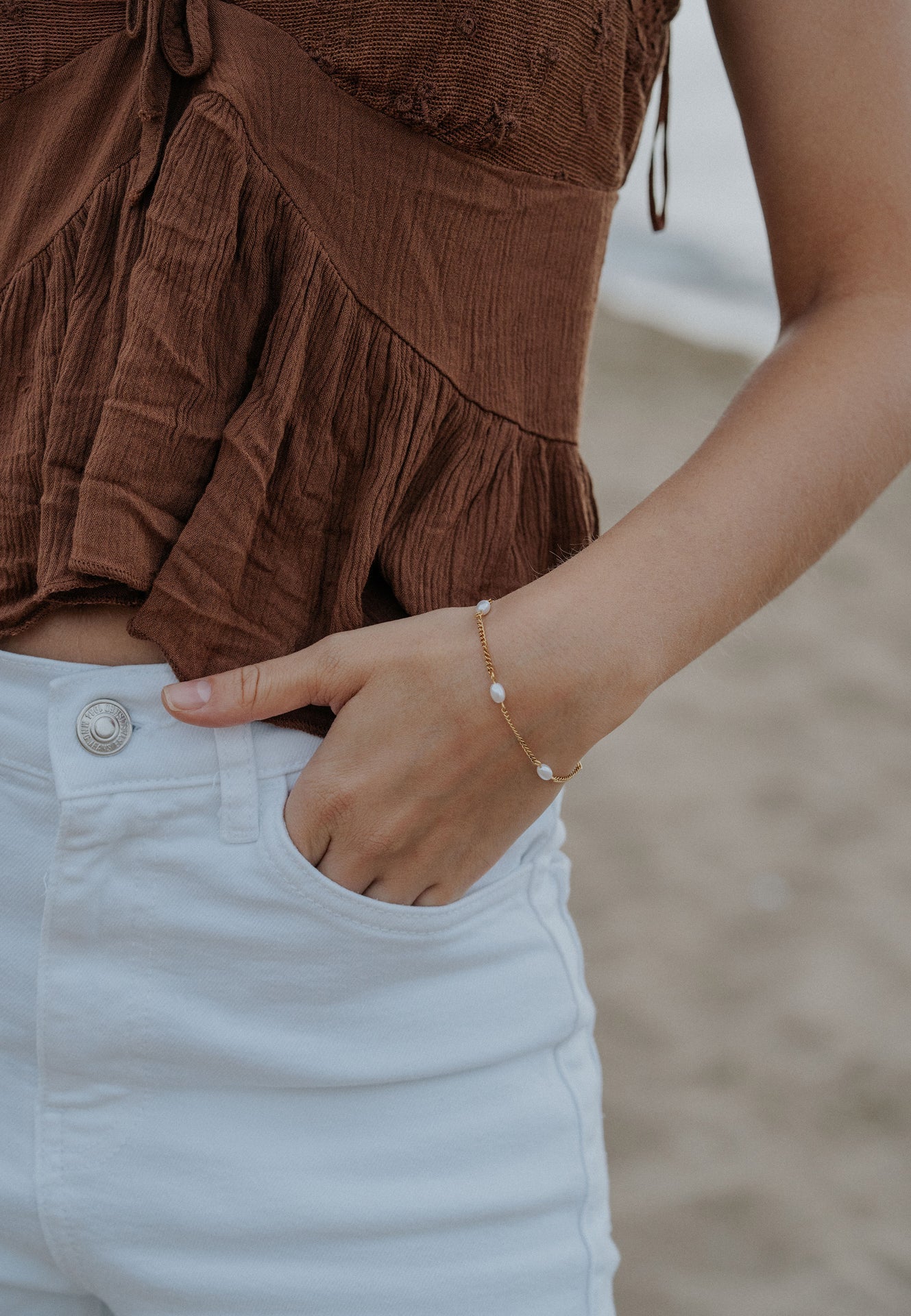 Close-up of a person wearing a brown textured top and white pants with a blurred background