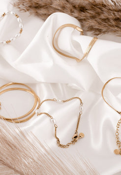 Gold jewelry including bracelets and necklaces on a white fabric background