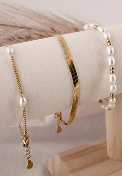 Gold and pearl jewelry set on a wooden stand with a neutral background