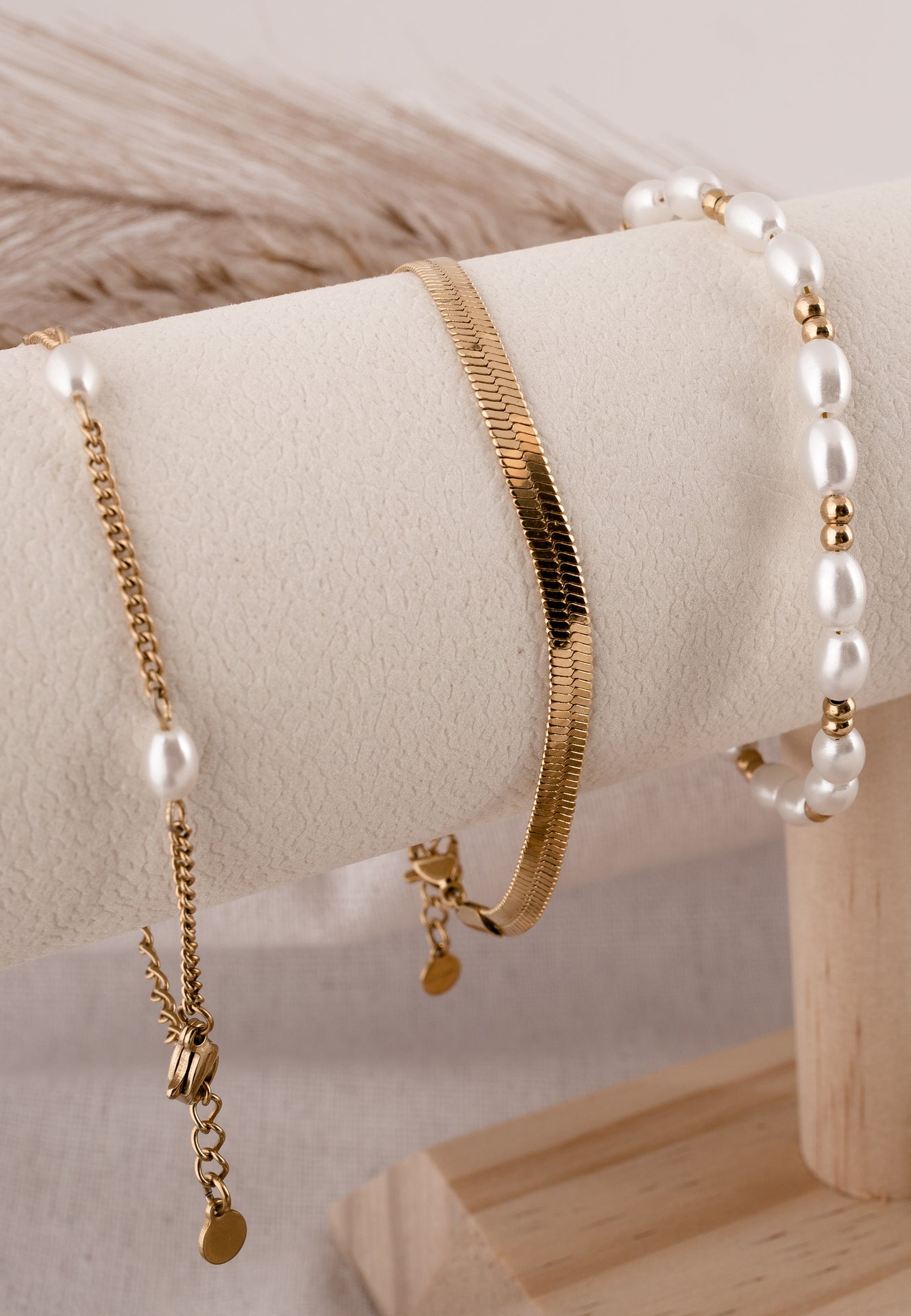 Gold and pearl jewelry set on a wooden stand with a neutral background