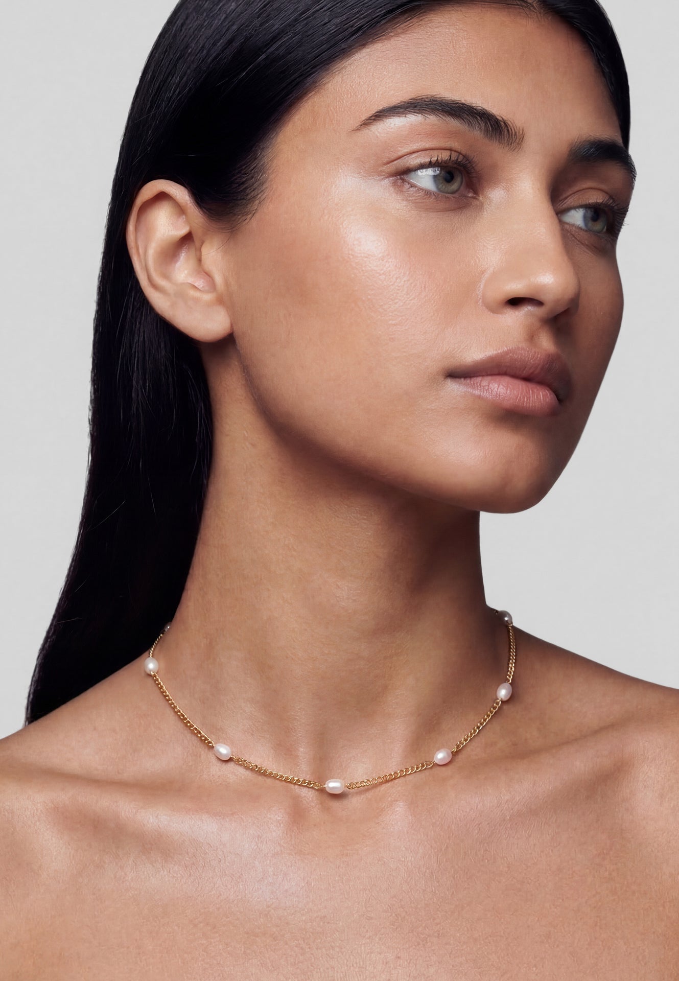Woman wearing a delicate necklace with pearls against a neutral background