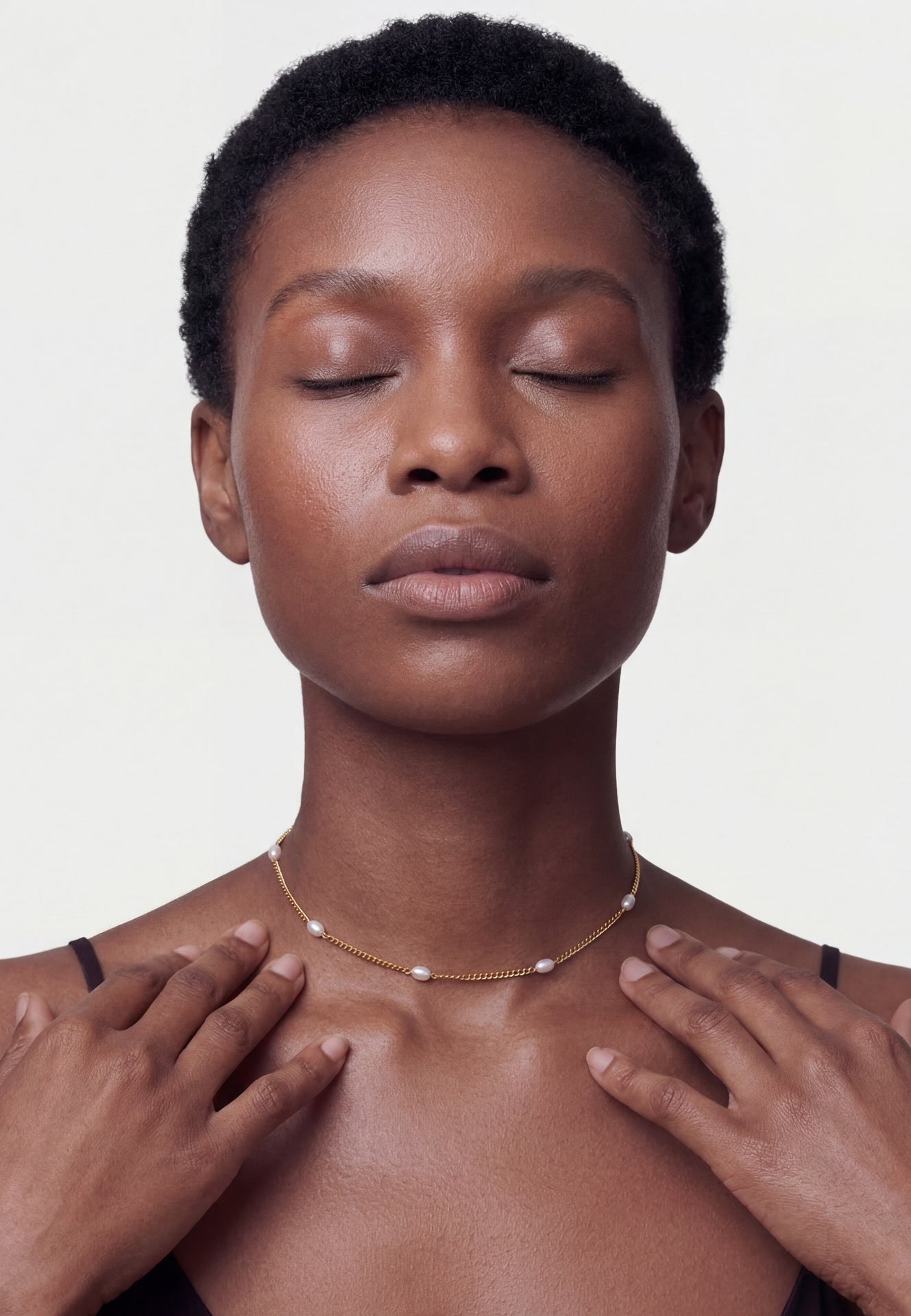 Woman with closed eyes wearing a delicate necklace on a plain background