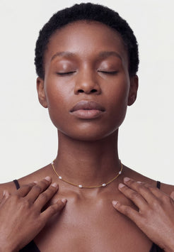 Woman with closed eyes wearing a delicate necklace on a plain background