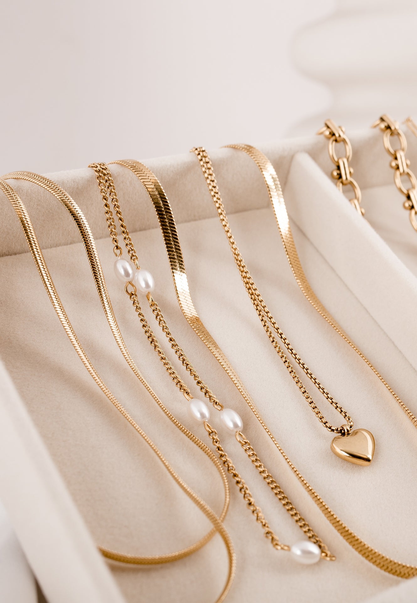 Gold necklaces with heart and pearl pendants on a white surface