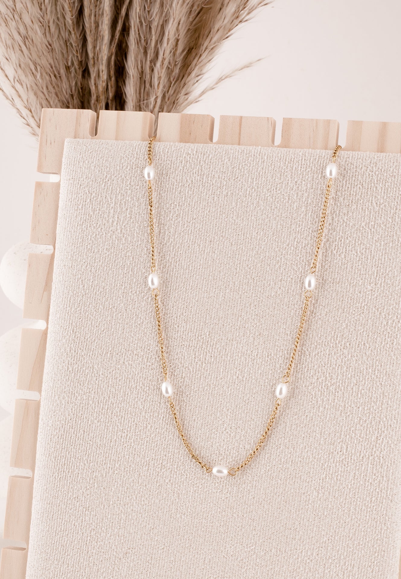 Gold necklace with pearls on a beige card, with dried plants in the background