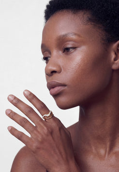 Close-up of a person with a gold ring on their finger against a neutral background