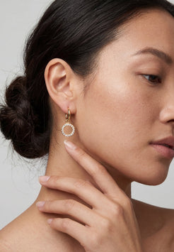 Close-up of a woman wearing gold hoop earrings with small round stones.