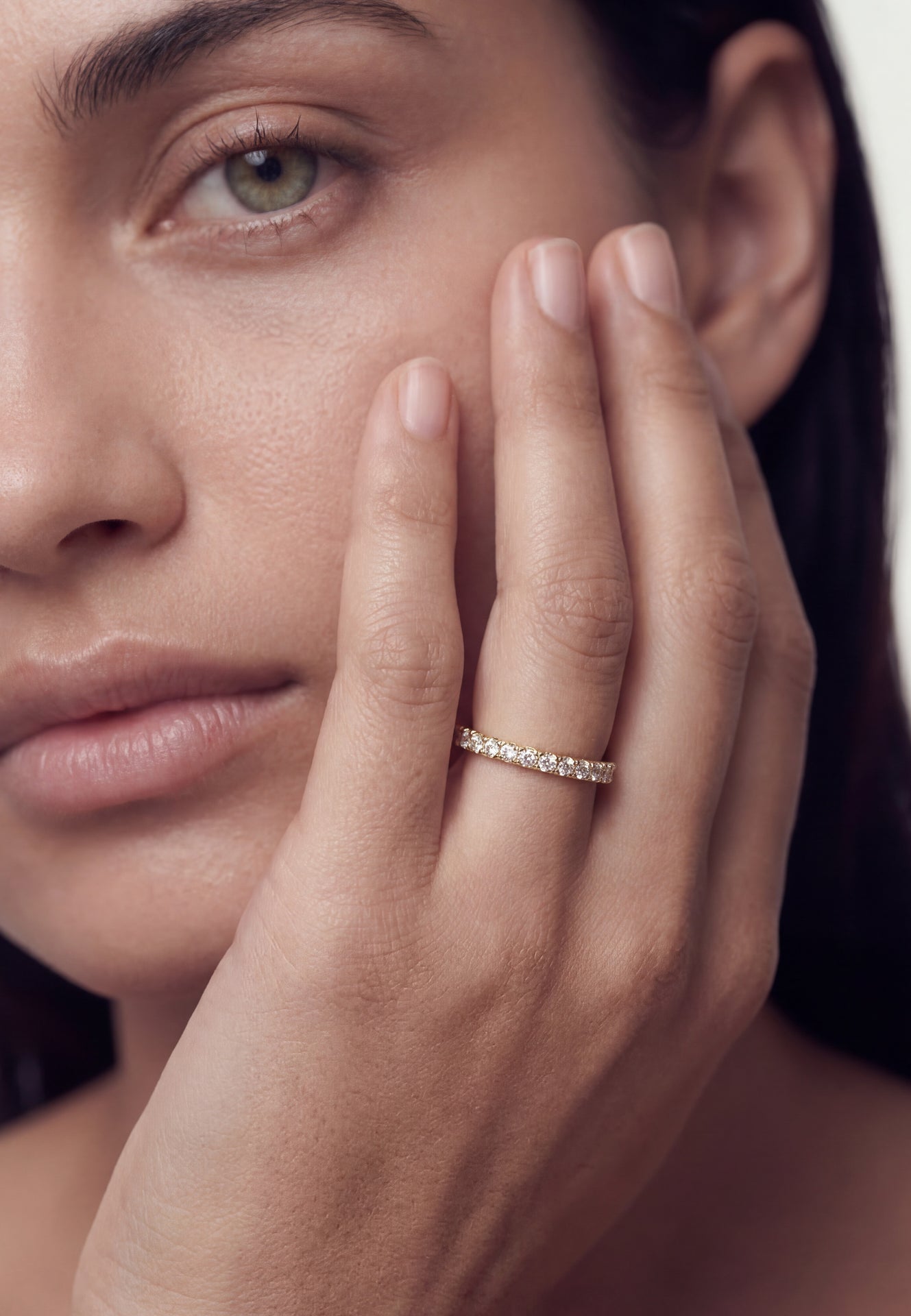 Close-up of a woman's hand with a ring on her finger, touching her face.