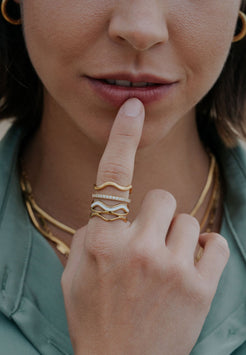 Close-up of a person wearing gold rings on their finger and hand, with a blurred background.