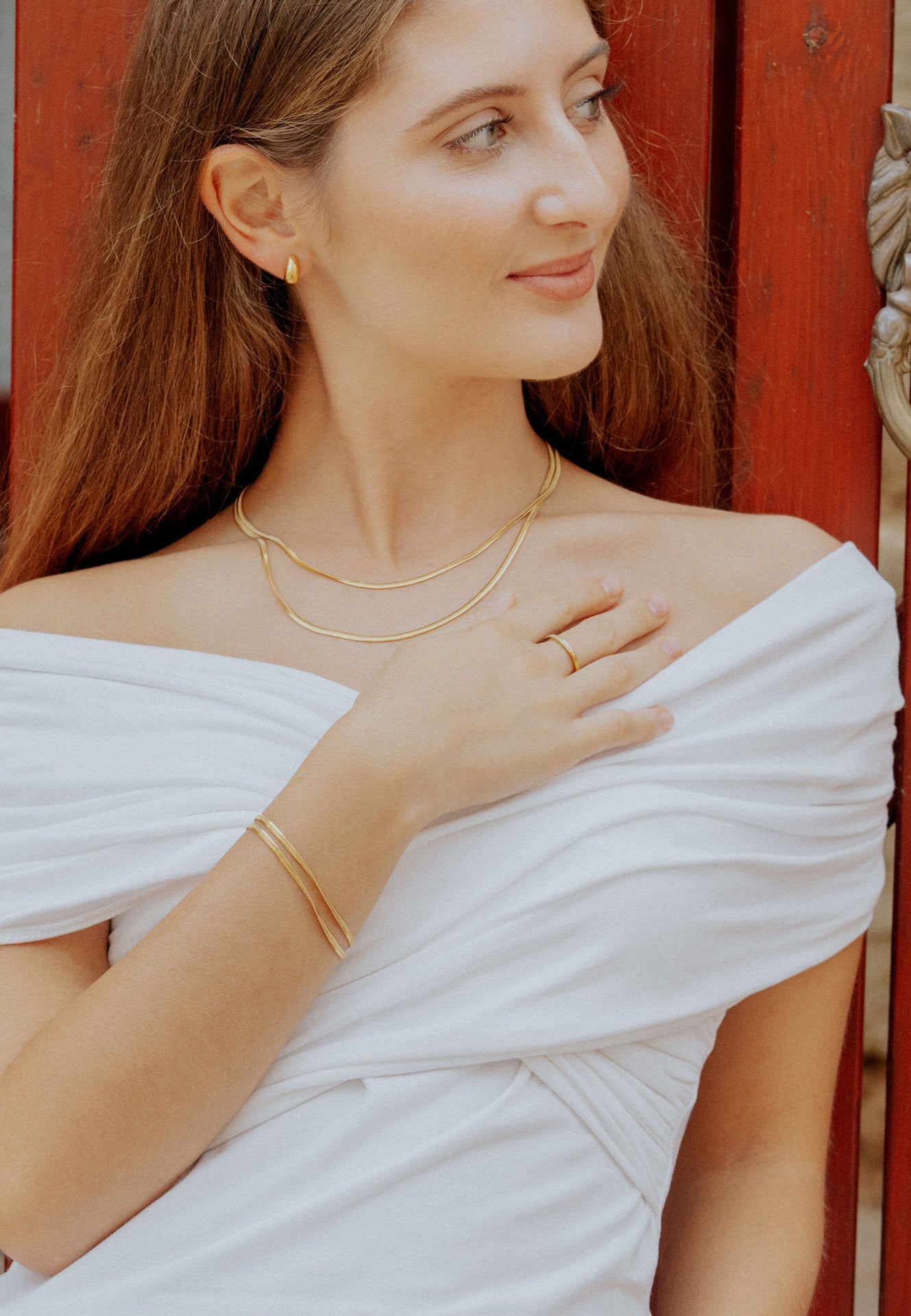 Woman wearing gold jewelry against a red wooden background