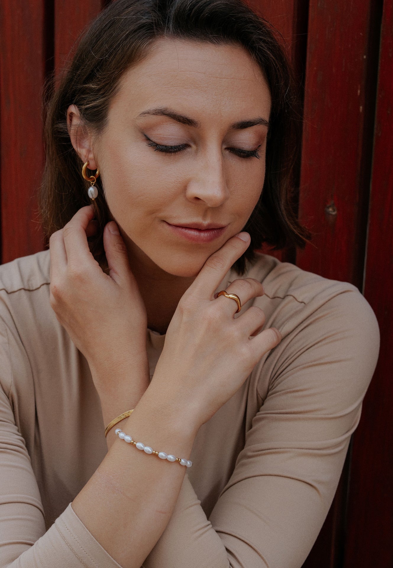 Woman adjusting her necklace against a red background