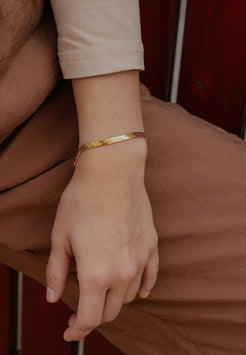 Close-up of a hand wearing a gold bracelet on a brown background