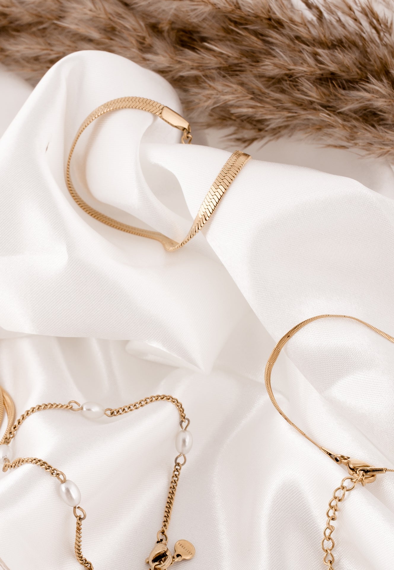 Gold jewelry including necklaces and bracelets on a white fabric background