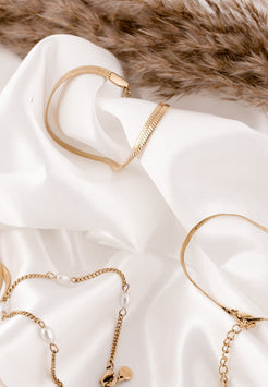 Gold jewelry including necklaces and bracelets on a white fabric background