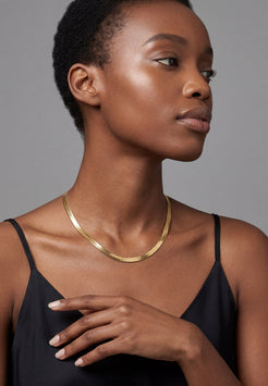 Woman wearing a gold necklace against a gray background
