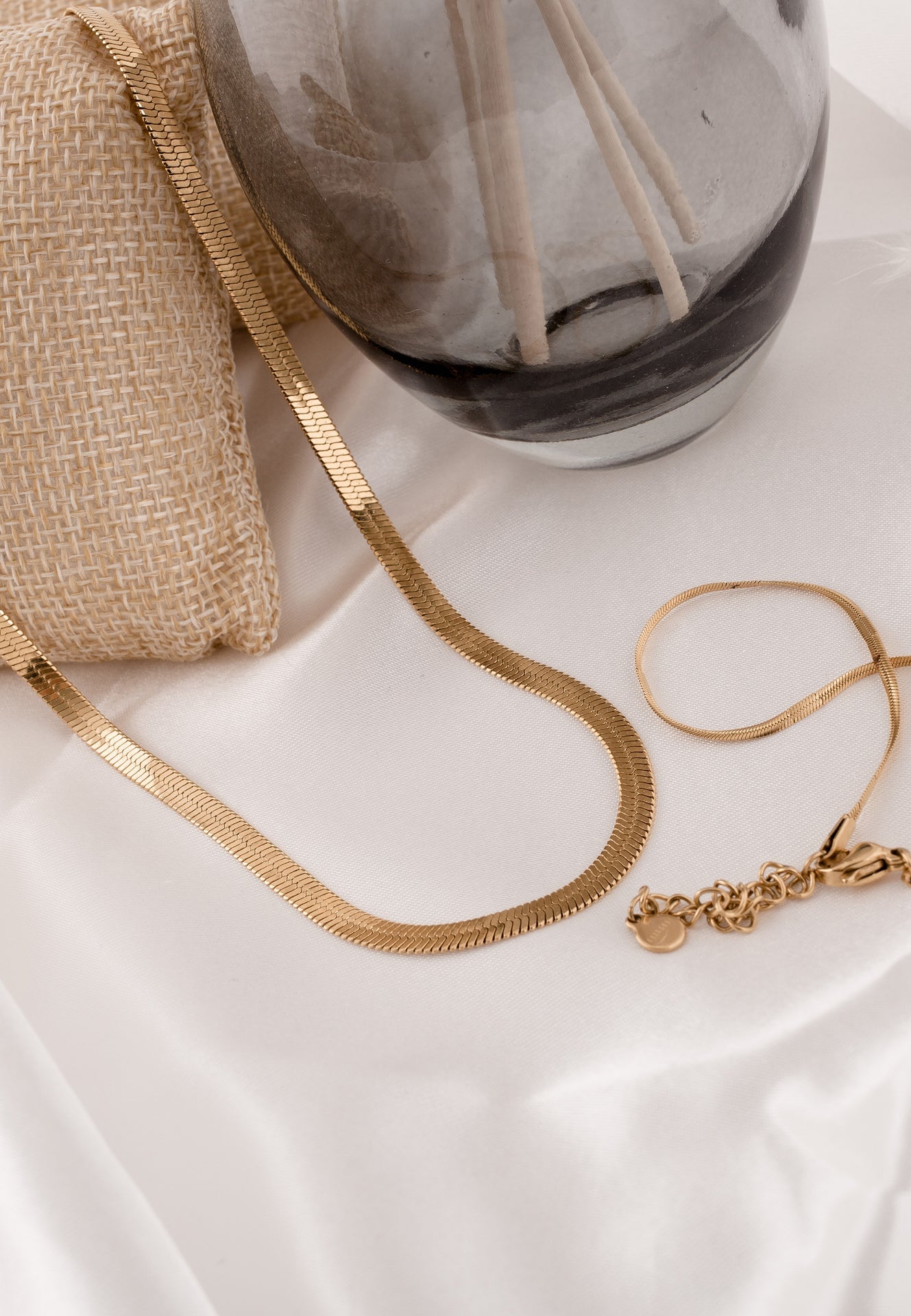 Gold necklace and bracelet on a white surface with a marble-patterned vase in the background.