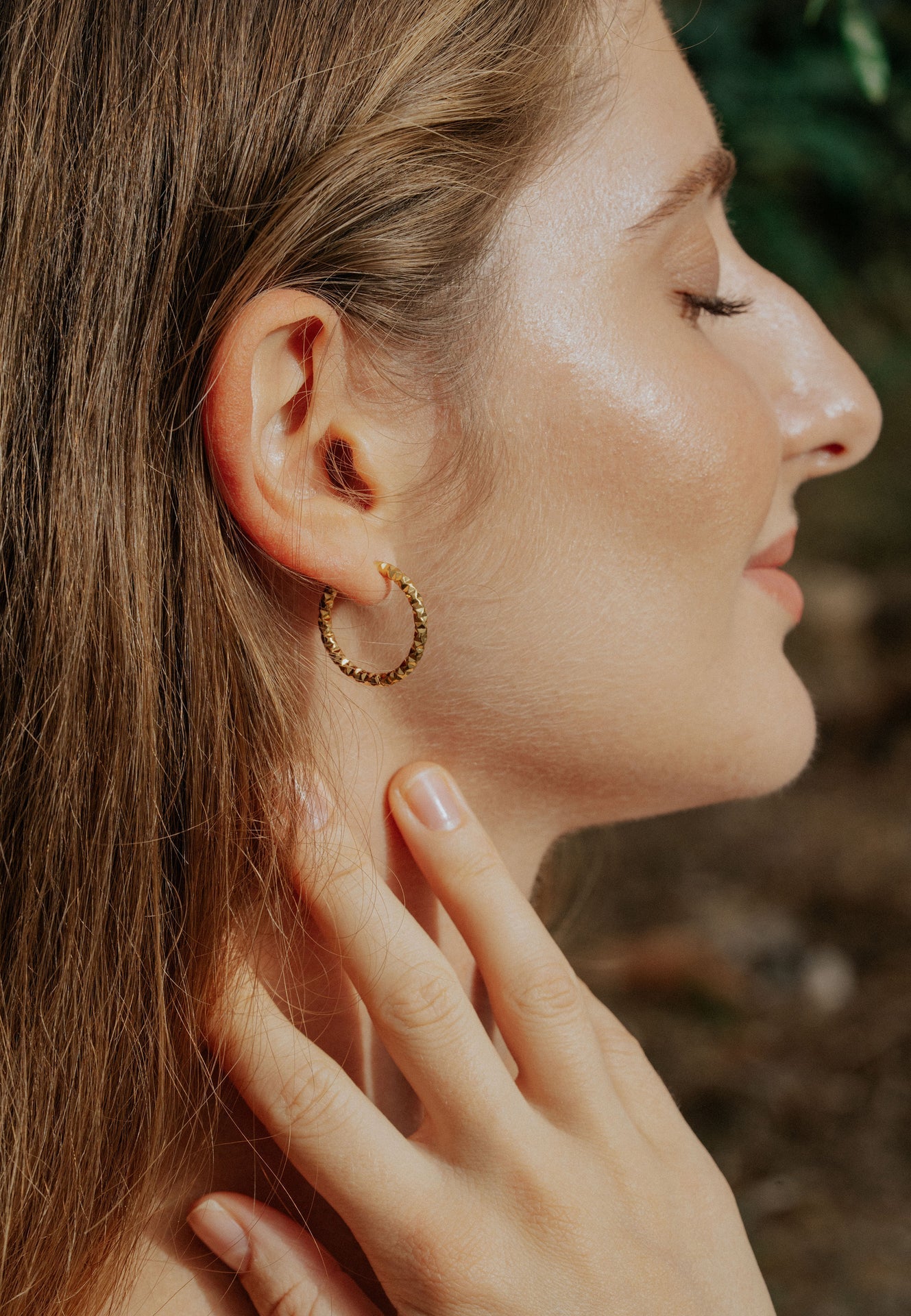 Close-up of a woman wearing gold hoop earrings with a blurred natural background