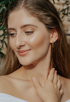 Woman with a soft smile, wearing gold earrings, with a blurred natural background