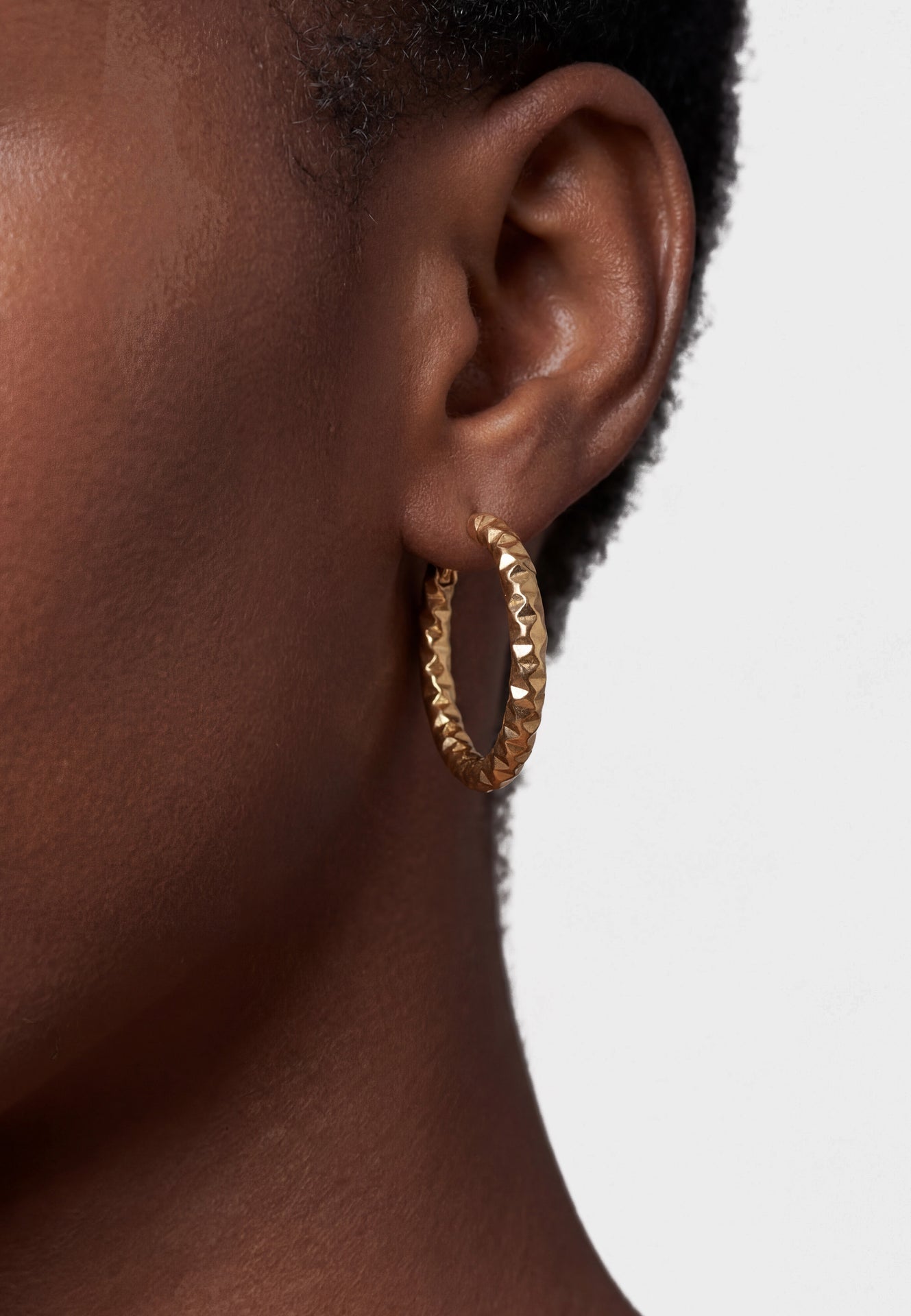 Gold hoop earring worn by a person with a neutral background