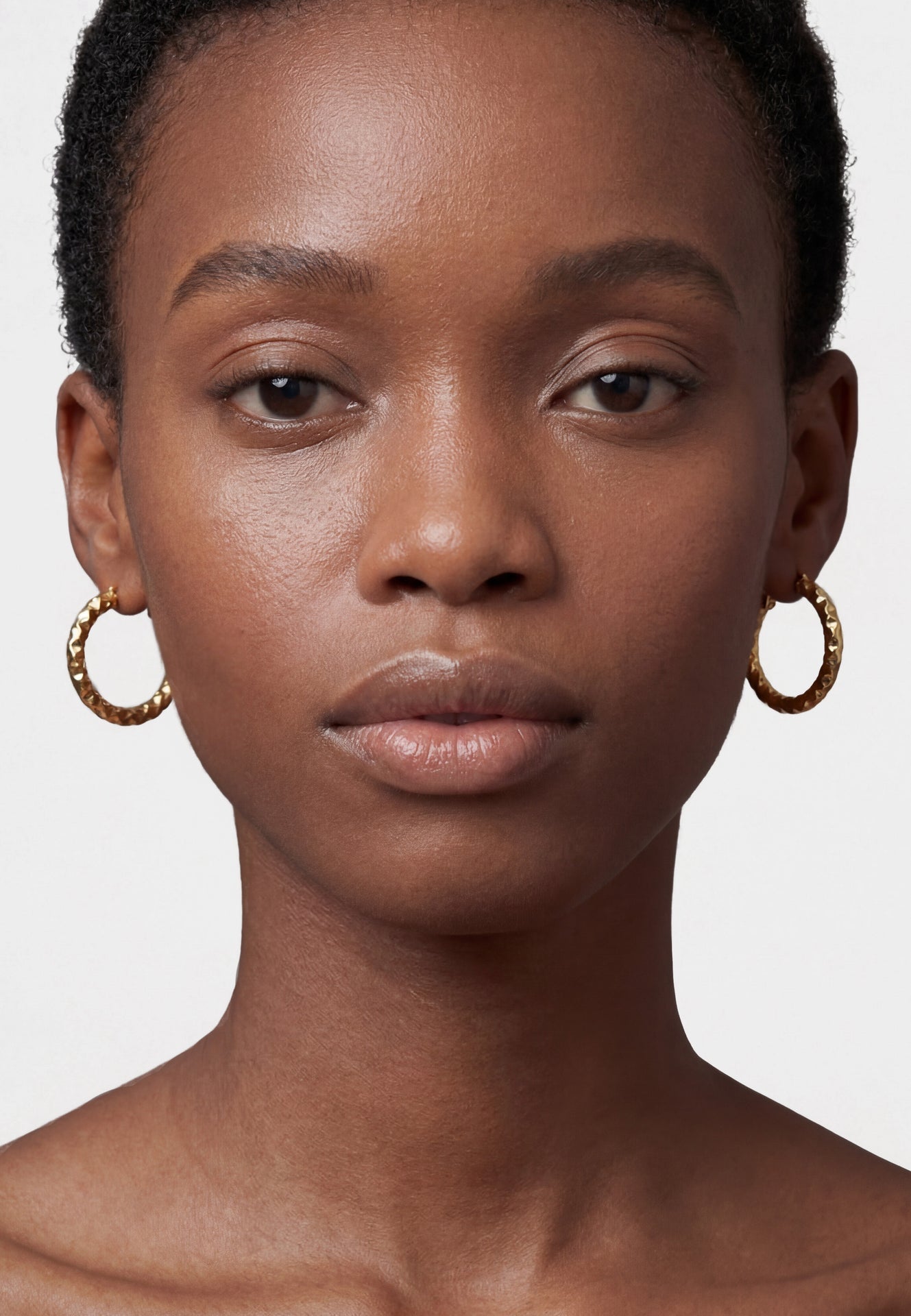 Close-up of a woman wearing gold hoop earrings against a neutral background