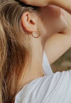 Close-up of a person wearing gold hoop earrings with a blurred background