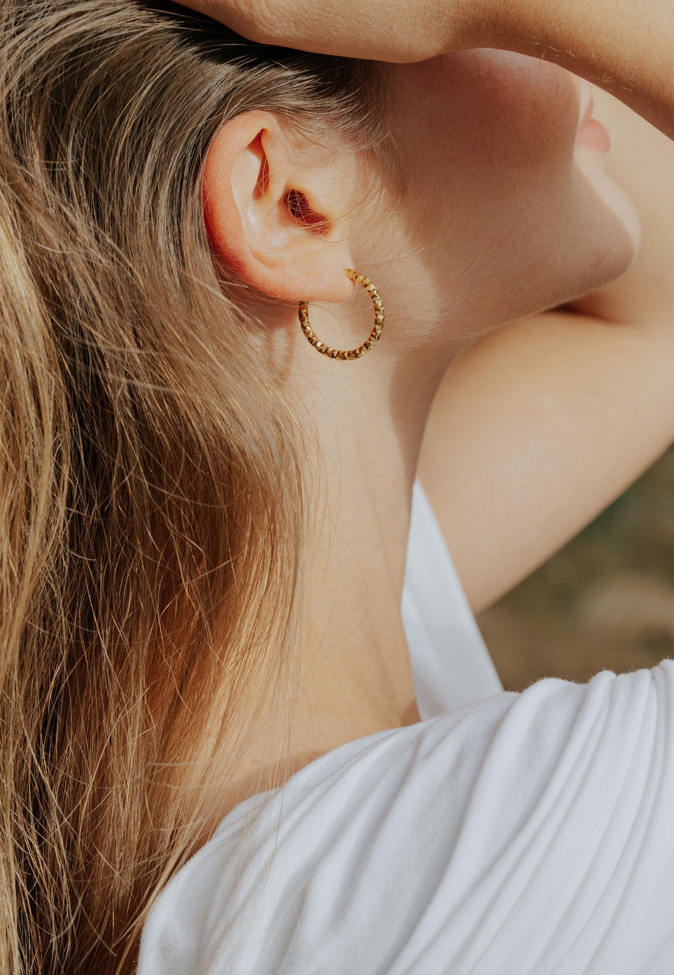 Close-up of a person wearing gold hoop earrings with a blurred background