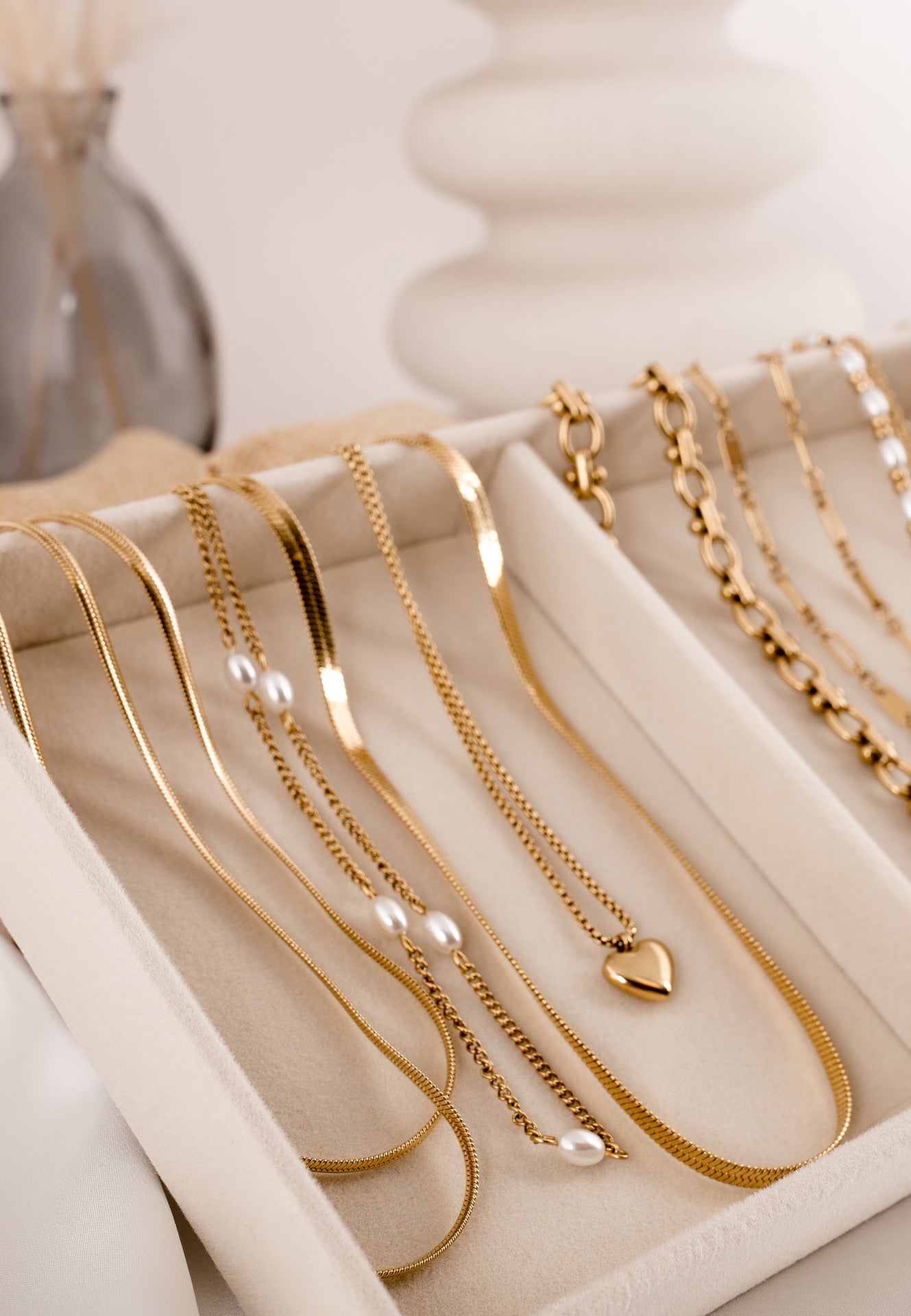 Gold necklaces displayed on a white tray with a soft focus background