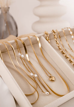 Gold necklaces displayed on a white tray with a soft focus background