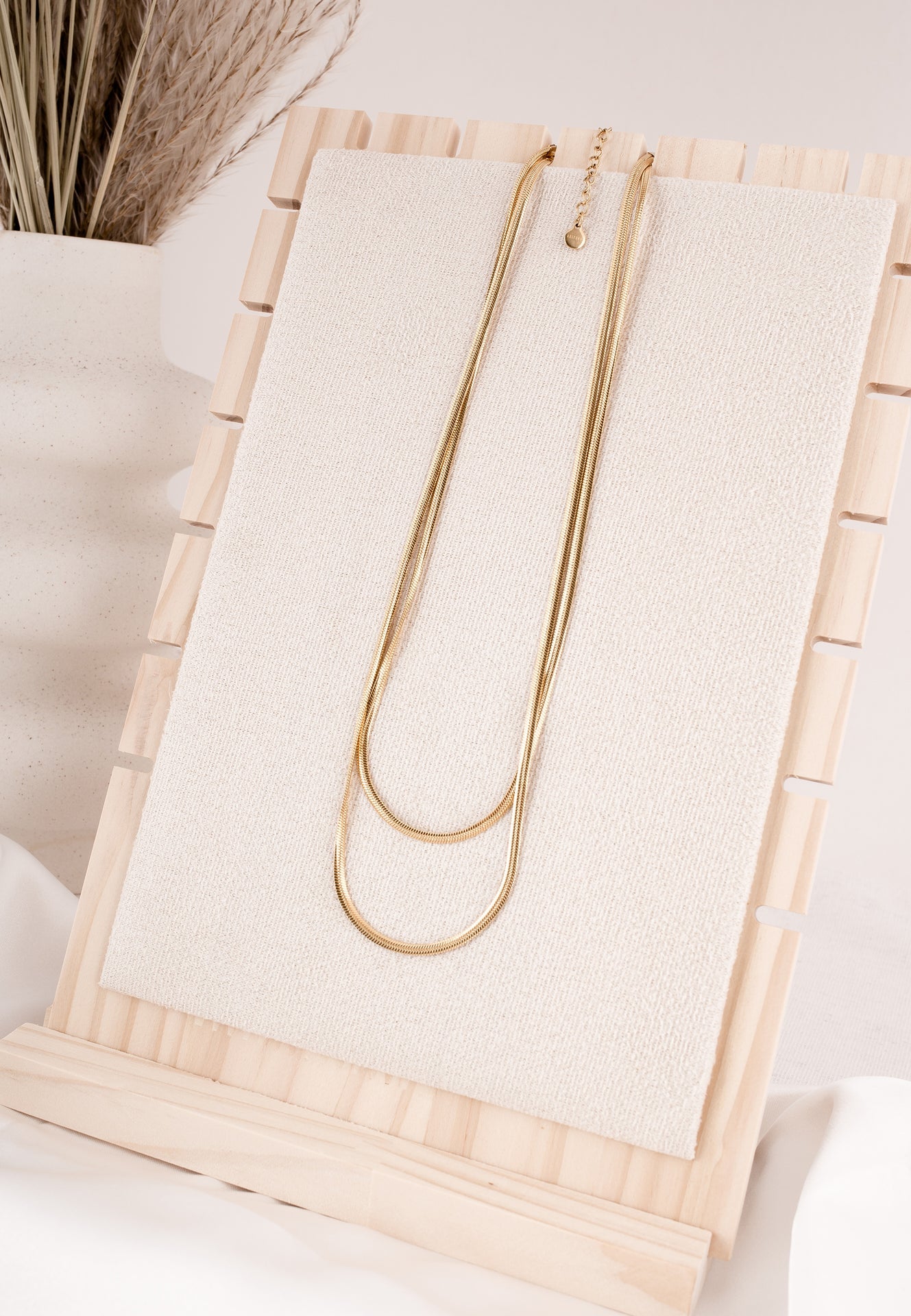 Gold necklace on a wooden stand with a neutral background