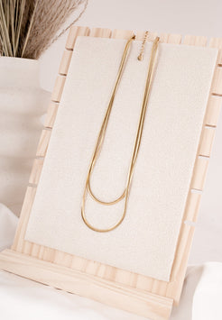 Gold necklace on a wooden stand with a neutral background