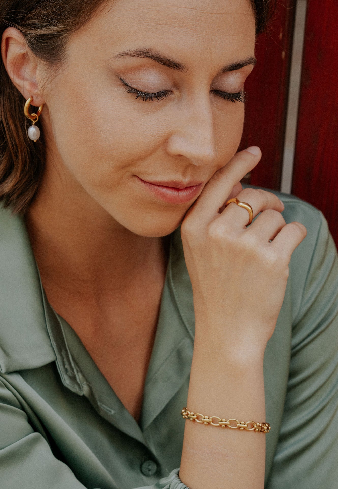 Woman wearing gold jewelry including earrings, ring, and bracelet, with a blurred background.