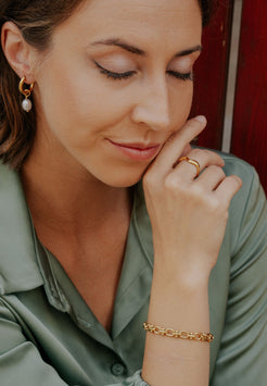 Woman wearing gold jewelry including earrings, ring, and bracelet, with a blurred background.
