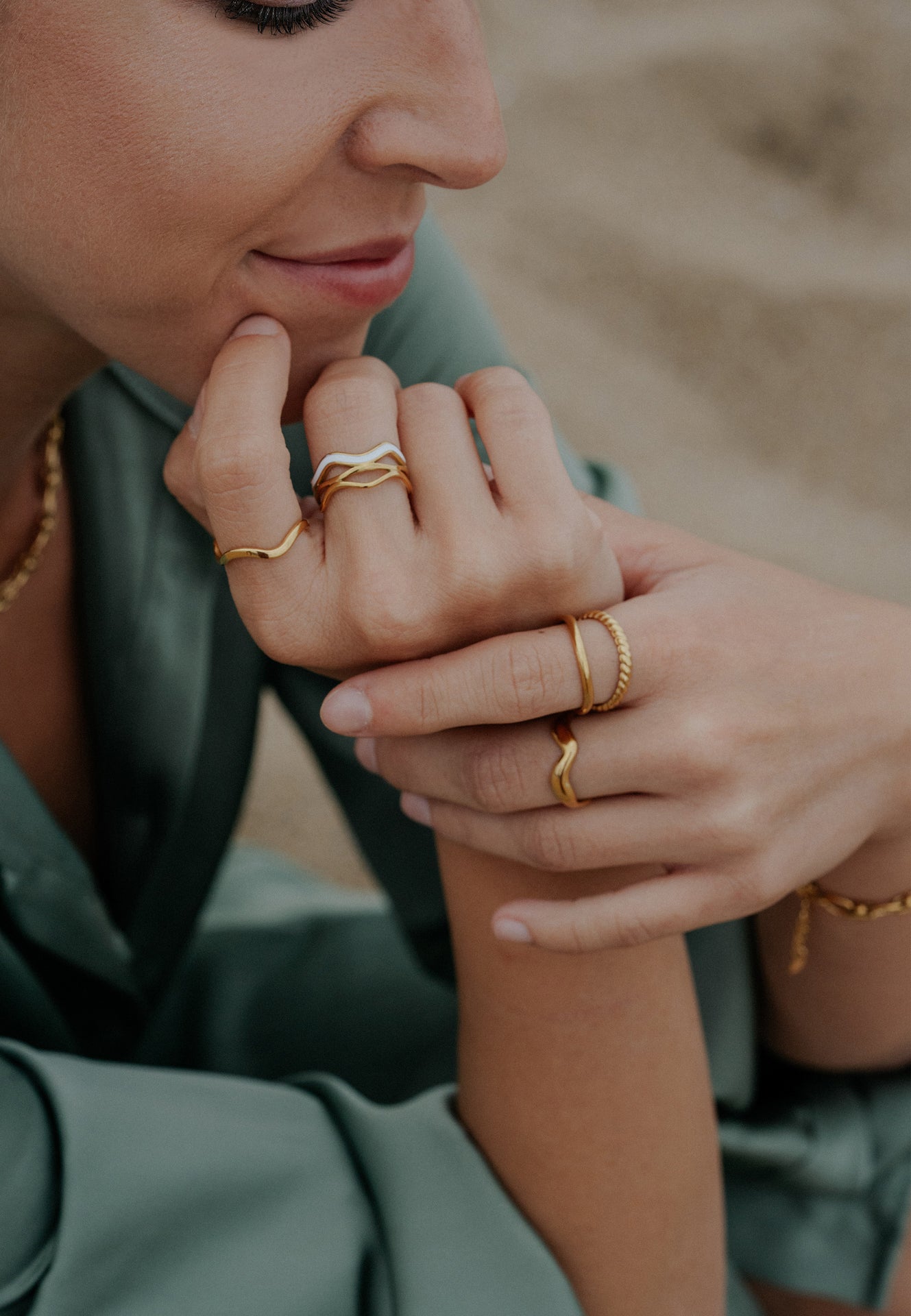 Close-up of a person wearing multiple gold rings on a blurred natural background