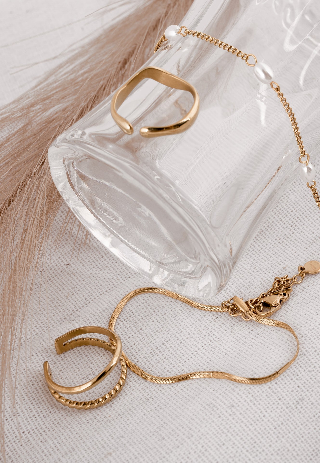 Gold bracelet and rings on a clear glass block with a light wooden background