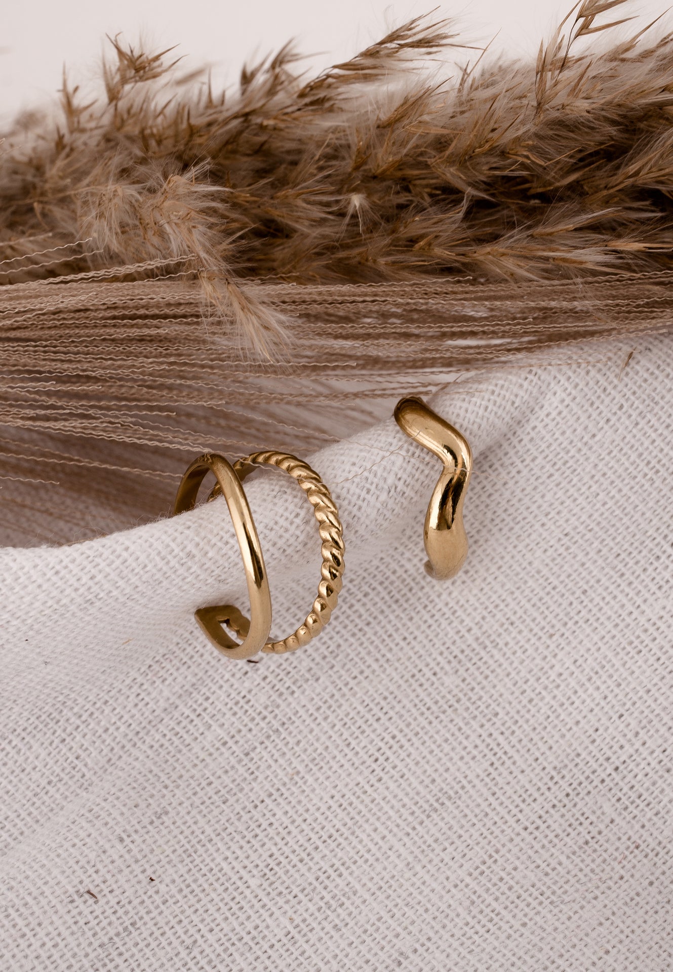 Two gold rings on a textured beige surface with dried pampas grass in the background.