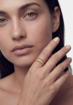 Close-up of a woman's face with a hand wearing gold rings on a neutral background
