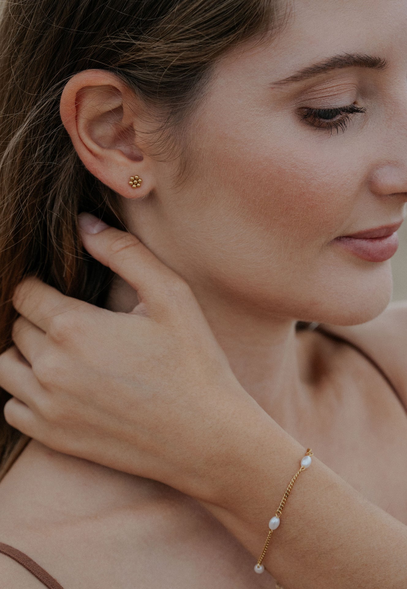 Woman wearing gold earring and pearl bracelet, close-up of face and hand.