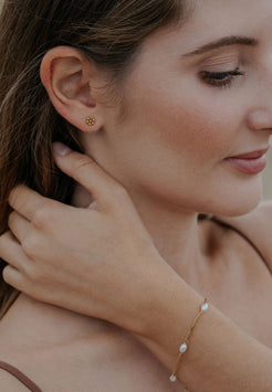 Woman wearing gold earring and pearl bracelet, close-up of face and hand.