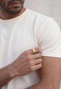 Man wearing a white t-shirt and gold ring on his finger, holding his arm.